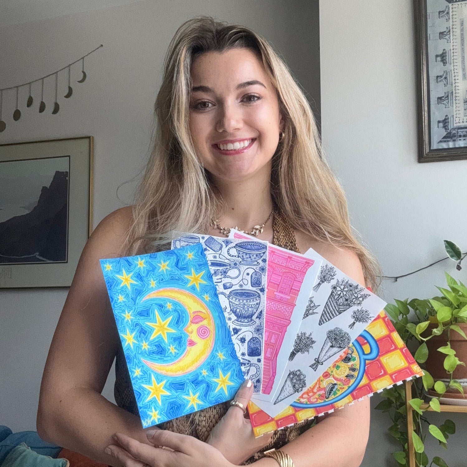Woman holding colorful art prints in a casual indoor setting